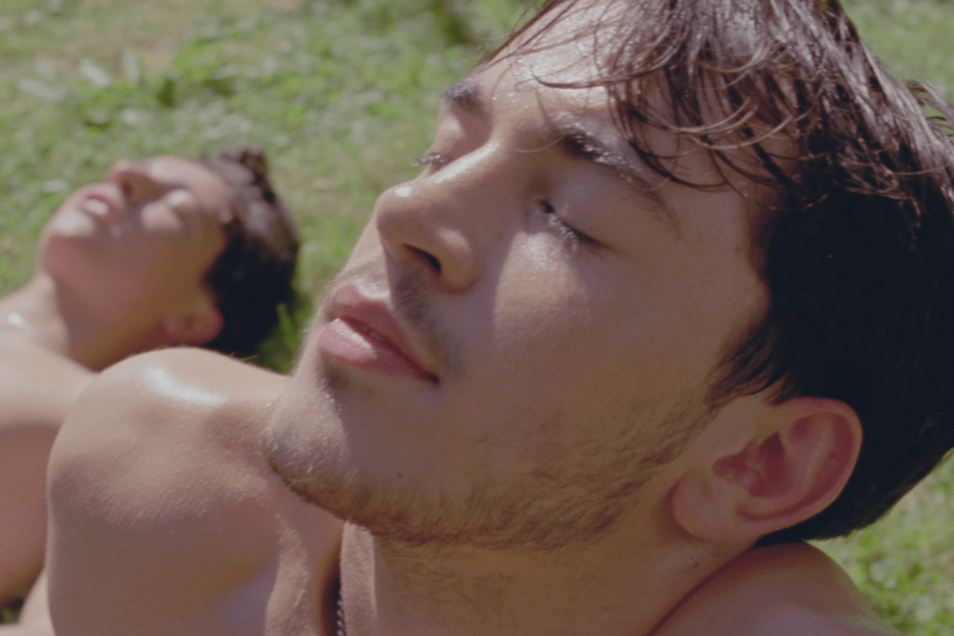 A young man basks in the sunshine, eyes closed, sitting on the grass.