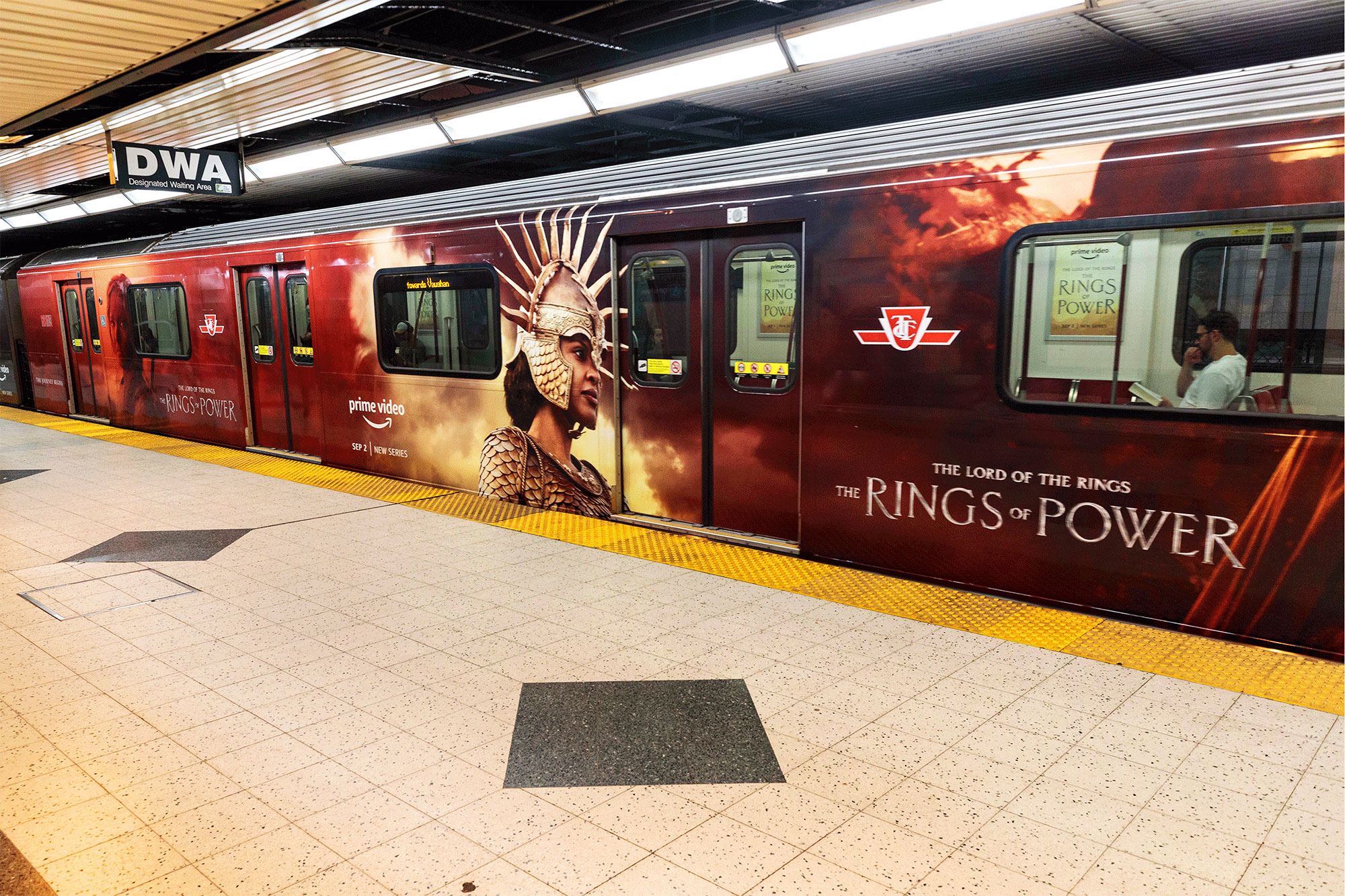 A bright red poster for 'Rings of Power' covering the side of a tube that has stopped at an underground platform.