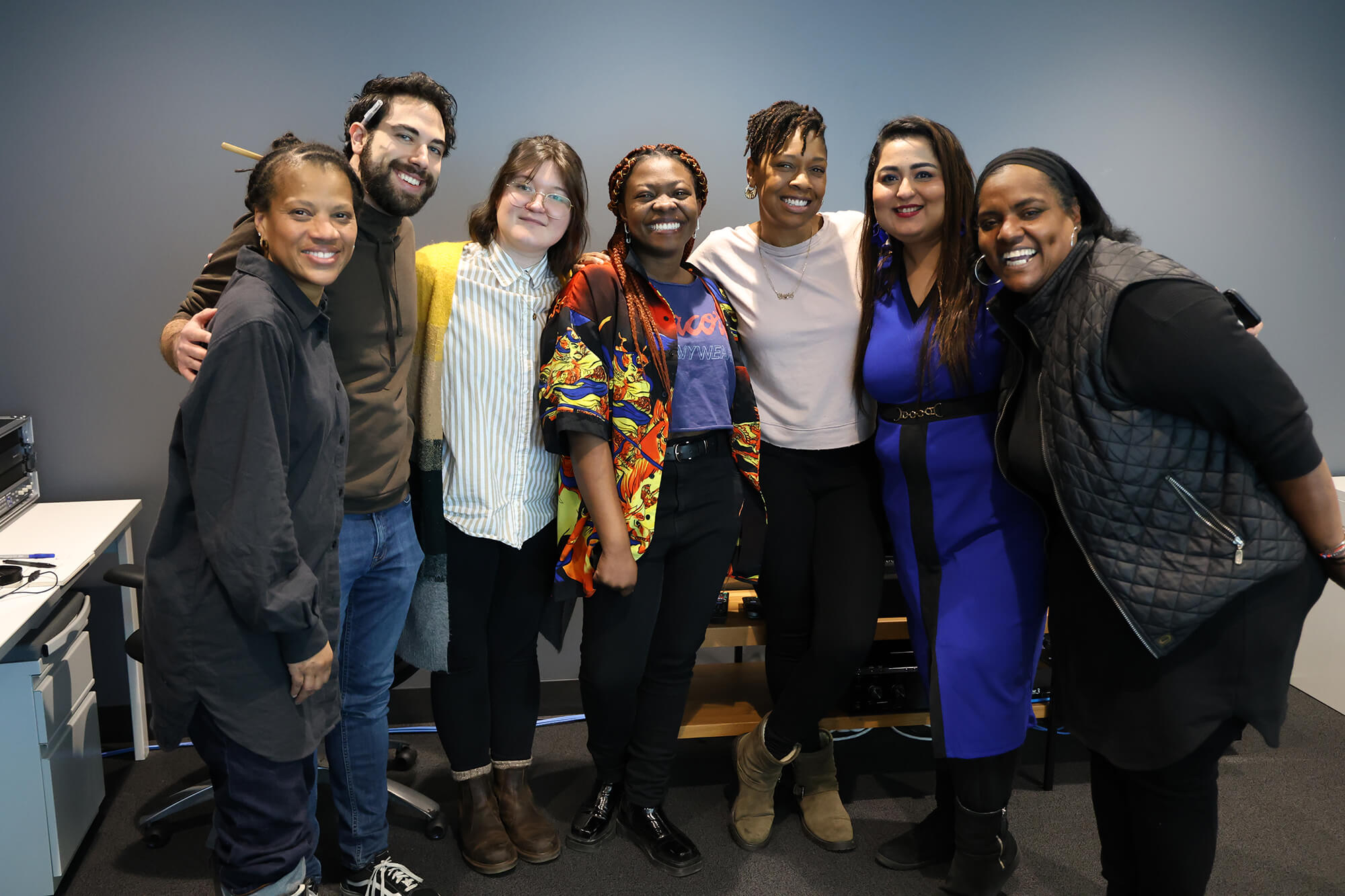 A group of diverse young people, consisting of six women and one man, smiling at the camera.