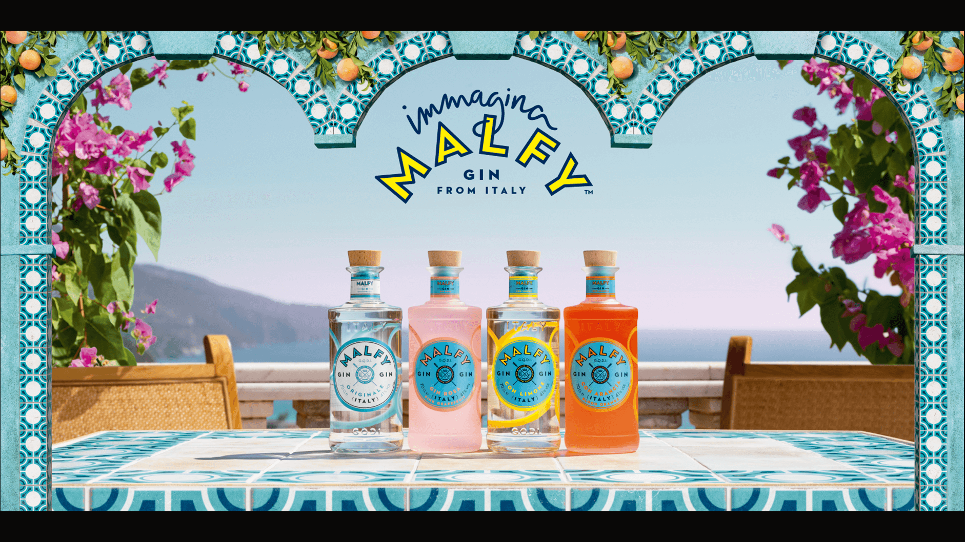 Four bottles of Malfy Gin are prominently displayed on a table, set against a coastal backdrop. The bottles are beautifully framed by intricate graphics of Mediterranean blue and white tiles, adding to the inviting and refreshing vibe of the scene.