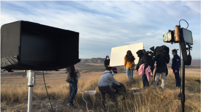 A production team is in a field with light but cloudy skies overhead.